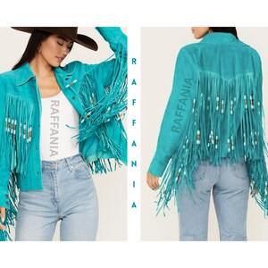 Puede incluir: Una chaqueta de ante color turquesa brillante con largos flecos en los paneles delanteros y traseros. Los flecos est&aacute;n adornados con peque&ntilde;as cuentas cil&iacute;ndricas en blanco, marr&oacute;n y turquesa. La palabra RAFFANIA est&aacute; impresa verticalmente.