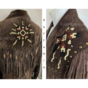 May include: A brown suede jacket featuring long fringe detailing along the back and shoulder yoke. The garment is adorned with intricate geometric beadwork in cream, red, and black, accented by a row of metallic studs along the yoke seam.