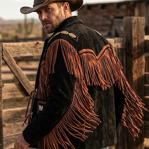 May include: Black suede jacket with long brown fringe detailing. The jacket features decorative stitching and is worn with a cowboy hat. The jacket is a western-style garment.