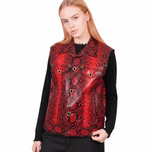 May include: A sleeveless vest featuring a vibrant red and black snakeskin pattern. The garment includes a pointed collar, a front button closure with metallic gold-toned hardware, and two chest pockets with buttoned flaps on the front panels.