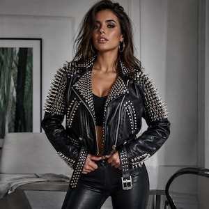 May include: A black leather jacket featuring silver-toned metal spikes and studs covering the shoulders, lapels, and sleeves. The jacket includes a front zip closure, a buckled belt at the waist, and silver metal hardware throughout the design.