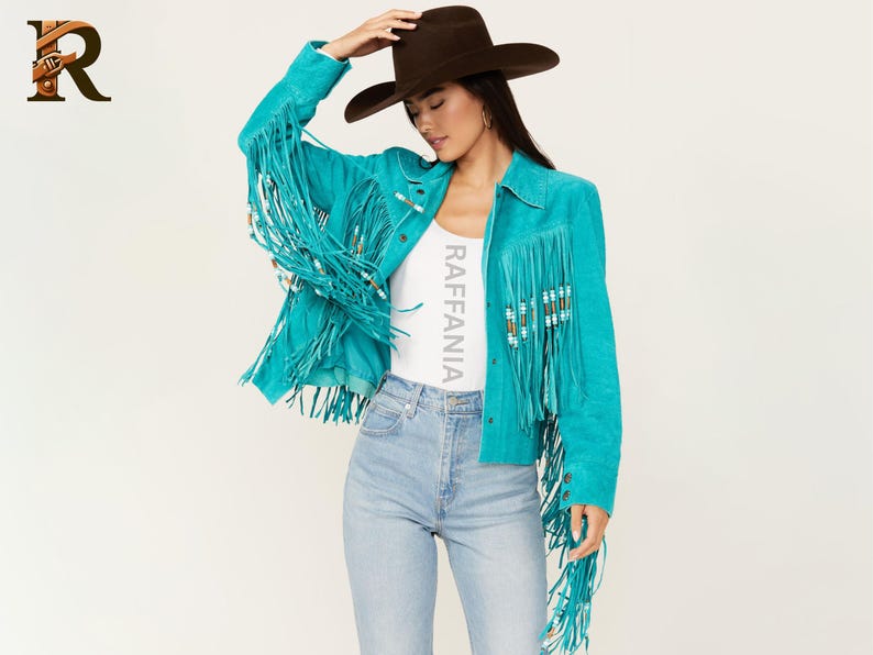 Puede incluir: Una chaqueta de ante color turquesa brillante con largos flecos en el pecho y las mangas, adornada con peque&ntilde;as cuentas cil&iacute;ndricas. La chaqueta se lleva sobre una camiseta blanca con el texto RAFFANIA impreso verticalmente en gris claro.