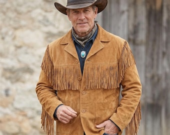 May include: A tan suede jacket featuring long fringe detailing across the chest, back, and sleeves. The jacket has a button-front closure, a notched collar, and two front pockets. It is worn with a dark blue shirt, a patterned neckerchief, and a brown hat.
