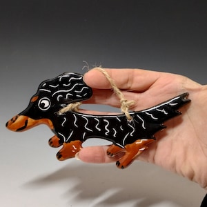 May include: Black and orange ceramic dachshund ornament with a white string for hanging.