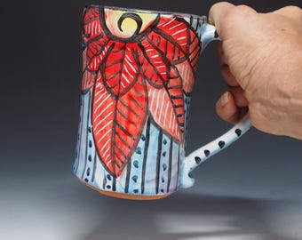 May include: A handmade ceramic mug with a blue and white striped background and a red and orange floral design. The mug has a handle with black polka dots.