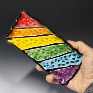 May include: A rainbow-colored ceramic dish with black outlines and a speckled pattern. The dish is shaped like a long rectangle with rounded edges.