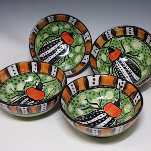 May include: Four ceramic bowls with a hand-painted insect design. Each bowl features a green interior with a black and white striped insect, an orange head, and a brown and orange striped rim. The bowls are arranged in a group.