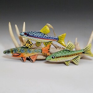 May include: Four ceramic fish ornaments with colorful designs. The fish have yellow, orange, and blue fins and tails. The fish are resting on a light-colored, antler-like structure.