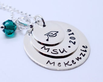 May include: Silver necklace with three layered discs. The top disc has a graduation cap, the middle disc says "MSU", and the bottom disc says "McKenzie . 2019". The necklace also has a green crystal bead.