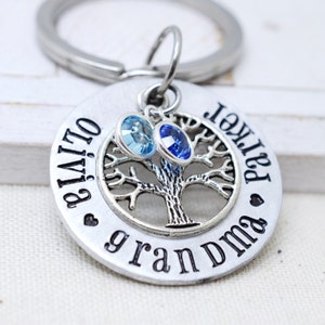 May include: Silver keyring with a tree design and two crystals, one blue and one light blue. The keyring also has the text "Olivia" and "Parker Grandma" engraved on it.