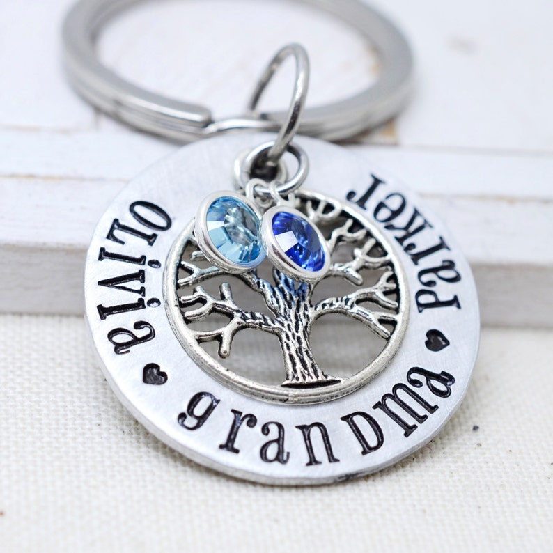 May include: Silver keyring with a tree design and two crystals, one blue and one light blue. The keyring also has the text "Olivia" and "Parker Grandma" engraved on it.