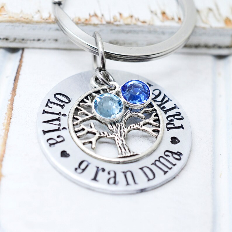 May include: Silver keyring with a tree design and two blue gemstones. The keyring is engraved with the text "Olivia & Patrick grandma".