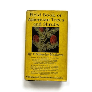 May include: A yellow book cover with a green evergreen tree illustration and red pine cones. The title is "Field Book of American Trees and Shrubs" by F. Schuyler Mathews.