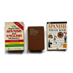 May include: Three small paperback books, all with Spanish language titles. The book on the left is red, white, and green and says "VOX Super-Mini Spanish and English Dictionary". The book in the middle is brown and says "Collins Spanish-English English-Spanish Dictionary". The book on the right is blue, white, and red and says "Dorling Kindersley Travel Guides Spanish Phrase Book".