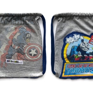 May include: Two grey drawstring bags with different designs. One bag features a cartoon image of Captain America with the words "America" and "Made in USA". The other bag features a cartoon image of Thomas the Tank Engine with the words "Day Out with Thomas" and "I Spent a Day Out with Thomas".