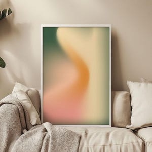 Op de afbeelding: Abstracte kunstprint met een wazig, draaiend ontwerp in tinten groen, oranje en roze. De print is ingelijst in een wit frame.