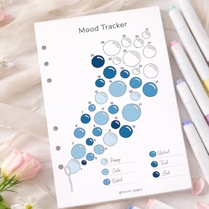 May include: A white mood tracker journal page with a bubble design, numbered 1-31, and color-coded for moods. The text "Mood Tracker" is at the top. Markers in various pastel colors are visible on the right.
