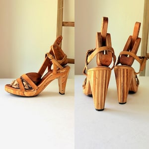 May include: Wooden platform sandals with a unique design. The sandals feature a light brown leather strap and a wooden heel. The heel is approximately 10 cm high. The sandals are displayed on a white surface.