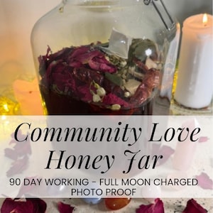 May include: A glass jar containing a dark liquid, dried rose petals, herbs, and spices. The jar is labelled "Community Love Honey Far" with text below. A lit white candle is in the background. The jar has a metal clasp.