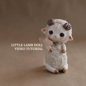 Peut inclure: Une poupée agneau artisanale avec un corps duveteux de couleur crème et un visage doux. La poupée a des yeux sombres, des joues roses et de petites cornes bouclées. Le texte "LITTLE LAMB DOLL VIDEO TUTORIAL" est visible.