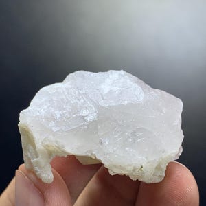 Può includere: Un cristallo bianco translucido con una texture ruvida e un gruppo di cristalli più piccoli. Il cristallo ha un aspetto naturale e grezzo.