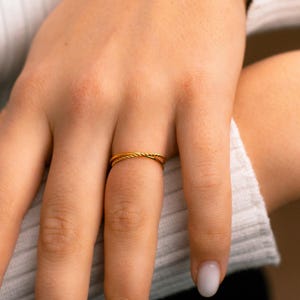 May include: A gold-colored ring with a twisted rope design. The ring is thin and delicate, and it is worn on a finger. The ring is a simple and elegant piece of jewelry.