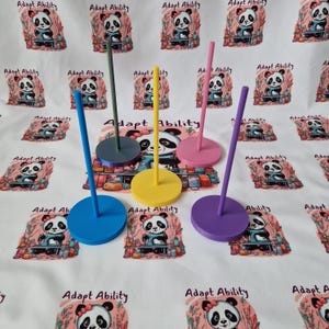 May include: A selection of colourful display stands in blue, green, yellow, pink, and purple. Each stand has a round base and a vertical pole. The background features a repeating pattern with panda illustrations and the text "Adapt Ability."