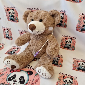 May include: A brown teddy bear with white paws and snout, and a medical tube attached. The background features a repeating pattern of a panda bear illustration with the text "Adapt Ability".