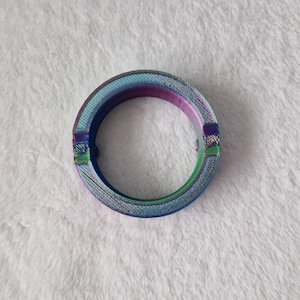 May include: A circular iridescent bracelet with a textured surface. The bracelet features a blend of colours, including blue, green, and purple. The bracelet has a clasp closure. The bracelet is approximately 6.35 cm in diameter.