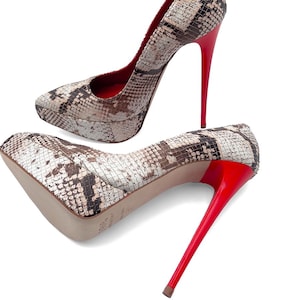May include: A pair of high-heeled platform pumps. The shoes have a snakeskin pattern in brown, beige, and black. The stiletto heels are bright red, as is the inner lining. The shoes are set against a white background.
