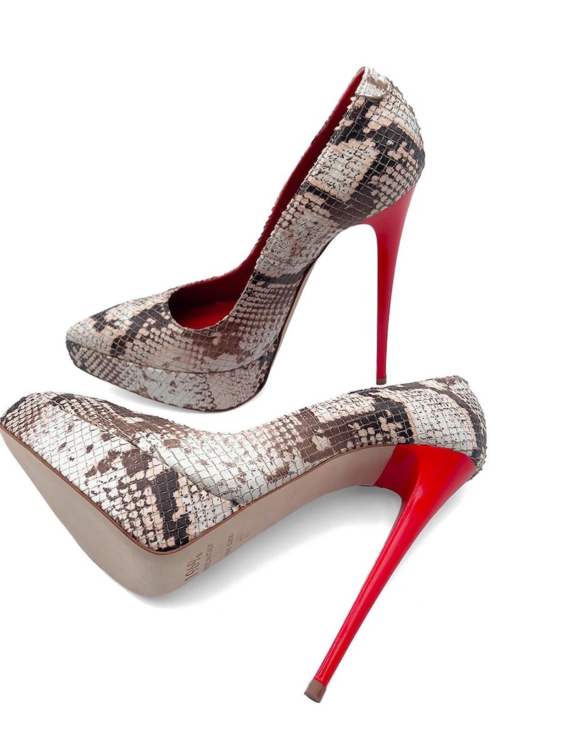 May include: A pair of high-heeled platform pumps. The shoes have a snakeskin pattern in brown, beige, and black. The stiletto heels are bright red, as is the inner lining. The shoes are set against a white background.