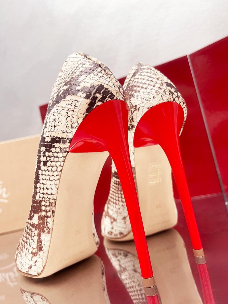 May include: A pair of high-heeled shoes with a snakeskin pattern in shades of brown and cream. The shoes feature bright red soles and stiletto heels, creating a striking contrast. The heels are approximately 4 inches tall.
