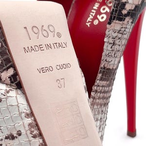 May include: Close-up of a high-heeled shoe with a snakeskin pattern. The sole is red, and the heel is thin. The insole is stamped with "1969 MADE IN ITALY VERO CUOIO" and size 37.