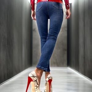 May include: Dark wash denim jeans and snakeskin print platform heels with red soles and stiletto heels. The outfit is completed with a red patent leather jacket and belt.