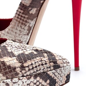 May include: Close-up of high-heeled shoes. The platform and upper feature a snakeskin pattern in brown, tan, and white. The stiletto heel is a bright red, contrasting with the neutral tones of the shoe.