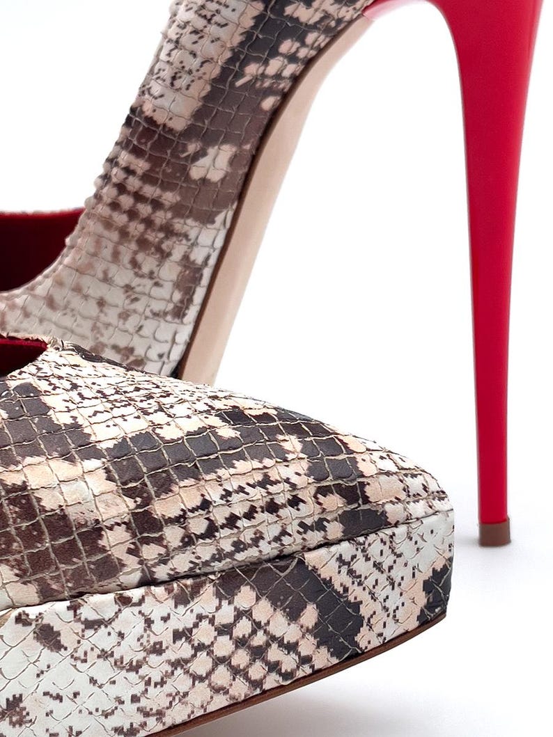 May include: Close-up of high-heeled shoes. The platform and upper feature a snakeskin pattern in brown, tan, and white. The stiletto heel is a bright red, contrasting with the neutral tones of the shoe.