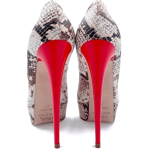 May include: A pair of high-heeled pumps with a snakeskin pattern in shades of brown, black, and cream. The heels are a vibrant red, and the shoes have a pointed toe design. The heels are approximately 12.7 cm tall.