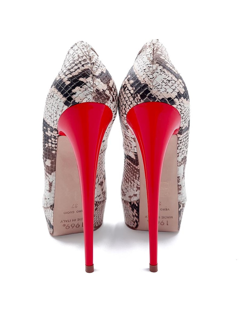 May include: A pair of high-heeled pumps with a snakeskin pattern in shades of brown, black, and cream. The heels are a vibrant red, and the shoes have a pointed toe design. The heels are approximately 12.7 cm tall.