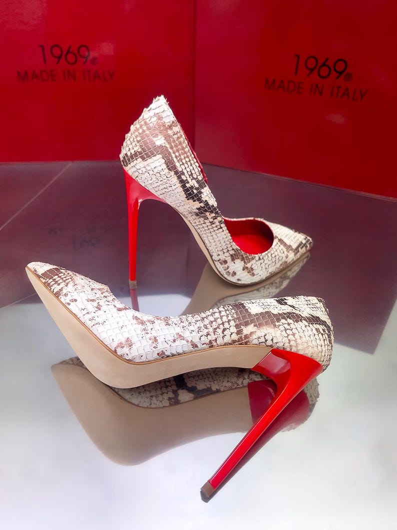 May include: A pair of high-heeled shoes with a snakeskin pattern in white, brown, and tan. The shoes have bright red heels and soles. The text "1969. MADE IN ITALY" is visible in the background.