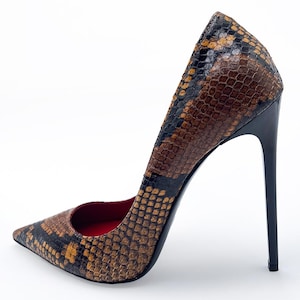 May include: A high-heeled pump with a pointed toe. The shoe features a snakeskin pattern in shades of brown, black, and gold. The heel is black and slender. The interior of the shoe is red.