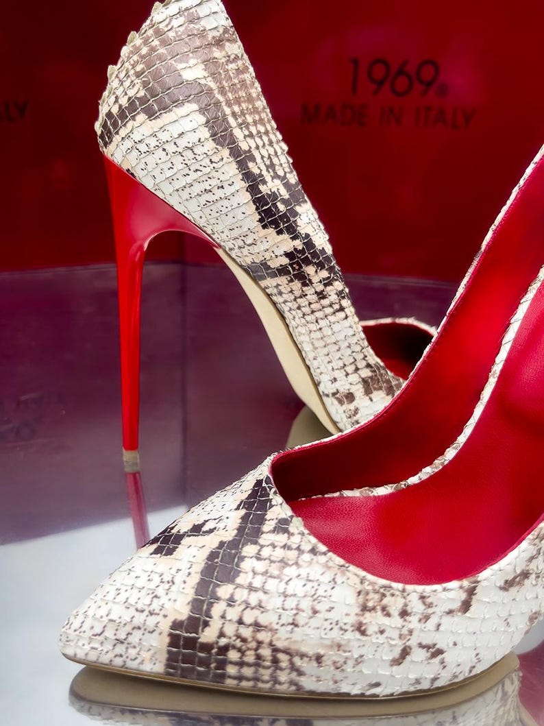 May include: A pair of high-heeled shoes with a snakeskin pattern in shades of white, brown, and black. The shoes have bright red soles and stiletto heels. The interior of the shoes is also red. The text "1969. MADE IN ITALY" is visible.