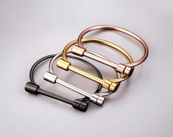 May include: Four bangle bracelets in different metal finishes: black, silver, gold, and rose gold. Each bracelet features a simple, minimalist design with a straight bar connecting two rounded ends.