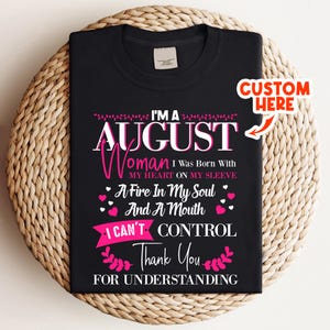 Op de afbeelding: Zwart T-shirt met een roze en witte afbeelding. De tekst luidt: "I'M A AUGUST Woman I Was Born With MY HEART ON MY SLEEVE A Fire In My Soul And A Mouth I CAN'T CONTROL Thank You FOR UNDERSTANDING."