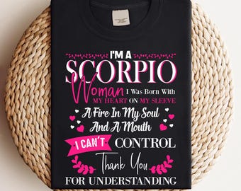 May include: Black t-shirt with the text "I'M A SCORPIO Woman I Was Born With MY HEART ON MY SLEEVE A Fire In My Soul And A Mouth I CAN'T CONTROL Thank You FOR UNDERSTANDING" in white and pink. The shirt is displayed on a woven surface.