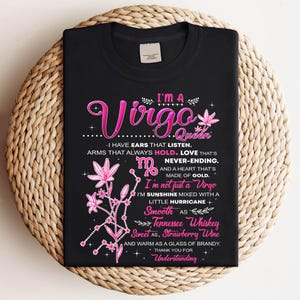 以下が含まれることがあります： ピンク色の「Virgo Queen」デザインの黒いTシャツ。グラフィックには、花のアクセント、乙女座のシンボル、乙女座の特性を説明するテキストが含まれています。シャツは織られた表面に表示されています。