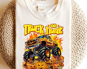 Puede incluir: Camiseta color crema con un diseño temático de Halloween. El diseño incluye un monster truck con llamas, las palabras "Truck or Treat" y calabazas de Halloween. La camiseta es de un material suave.