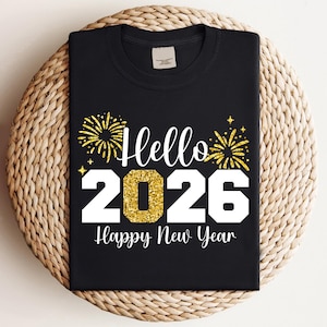 以下が含まれることがあります： 「Hello 2026 Happy New Year」の文字が白とゴールドのグリッターでプリントされた黒いTシャツ。デザインには、新年の祝賀に最適な、ゴールドのグリッターの花火と星が含まれています。