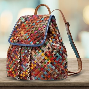 Può includere: Uno zaino in pelle intrecciata multicolore con patta e spallacci regolabili. La borsa presenta una varietà di colori, tra cui rosso, blu, giallo e verde. Ha una maniglia superiore e una chiusura con coulisse. La borsa è su una superficie di legno.
