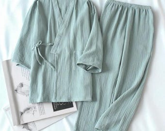 May include: A light green pajama set, including a long-sleeved wrap top with a tie closure and matching pants. The set is made of a textured fabric and is displayed on a white surface. A book with illustrations is partially visible.