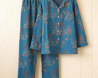 May include: A teal pajama set with a landscape pattern featuring trees and mountains. The long-sleeved button-down shirt and pants have orange trim. The set is hanging on a wooden hanger.